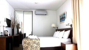A hotel room with a bed, bedside table, lamp, air conditioning unit, and a TV on a stand. - Ribera Sur Mar del Plata (Mar del Plata)