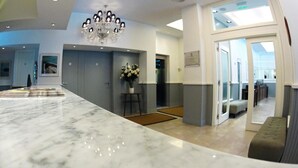 A modern hotel lobby with a marble reception desk, a chandelier, and a view of the dining area. - Ribera Sur Mar del Plata (Mar del Plata)