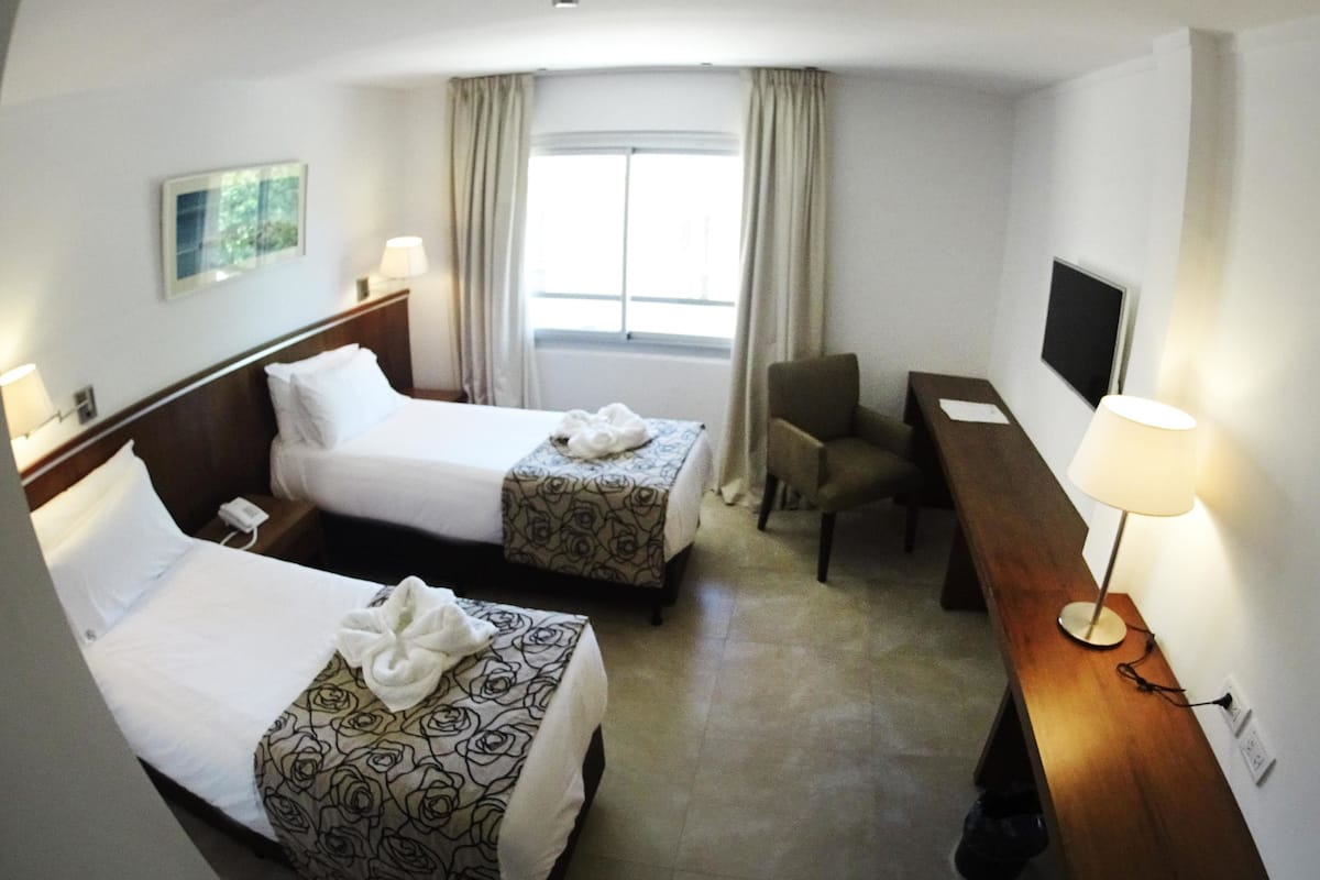 A hotel room with two beds, a desk, a chair, a TV, and a window with curtains.