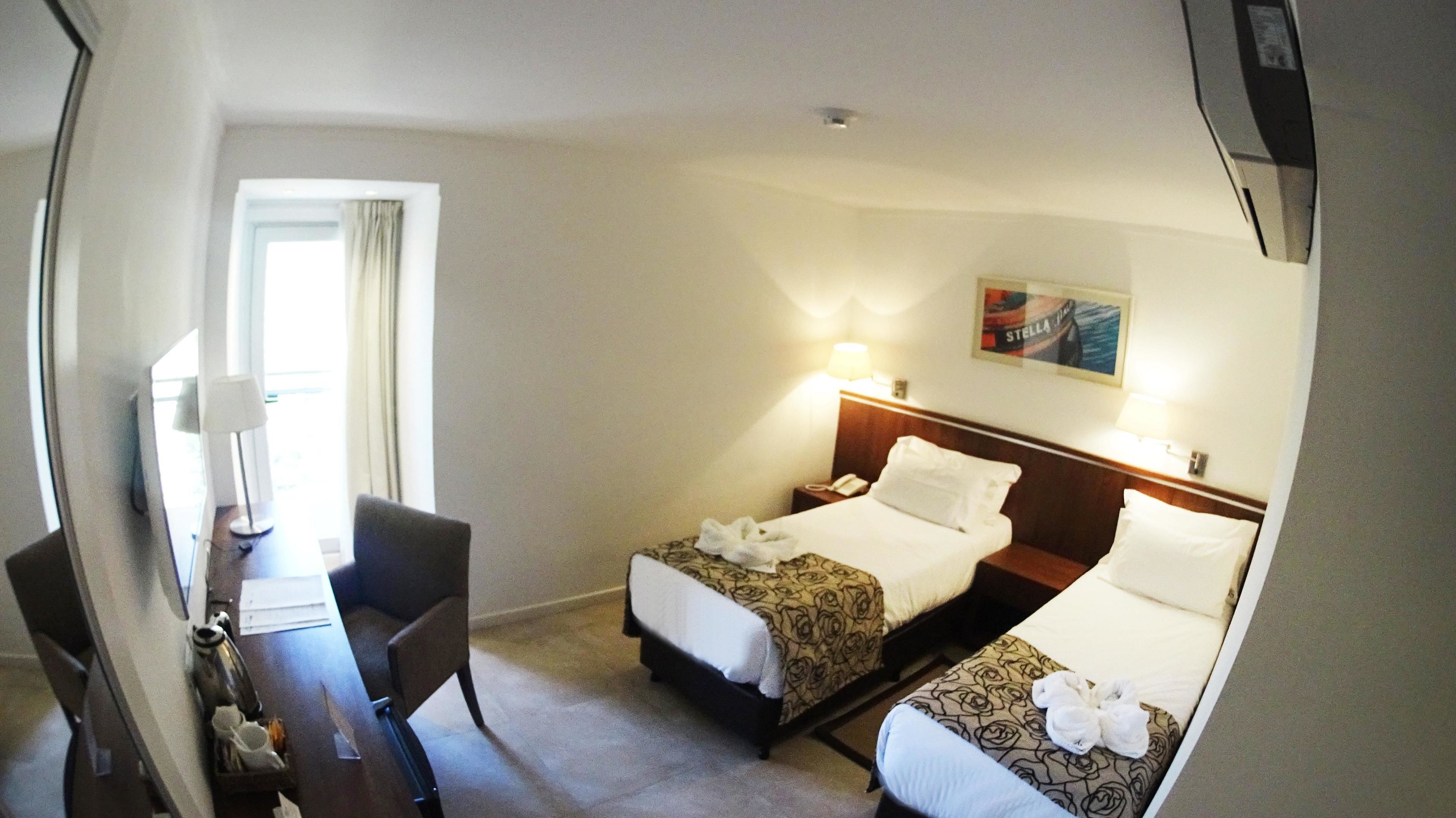 Habitación de hotel con dos camas, un escritorio, una silla y una ventana con cortinas.