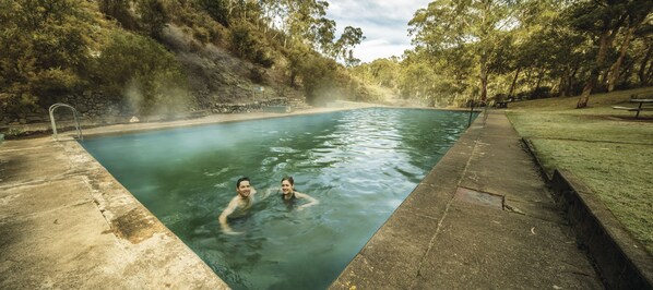 Ein rechteckiger Pool mit zwei Personen im Wasser, umgeben von einer Steinmauer und Bäumen.