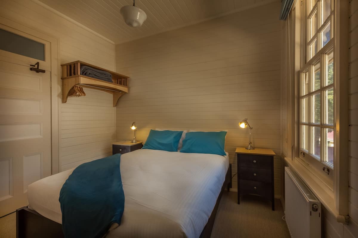 A bedroom with a bed, two bedside tables, a nightstand, a window, and a door.