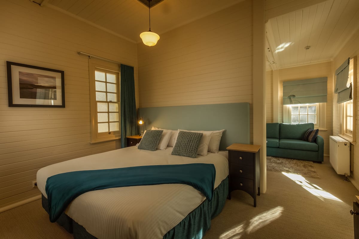 A bedroom with a large bed, a nightstand, a dresser, a window, and a blue sofa.