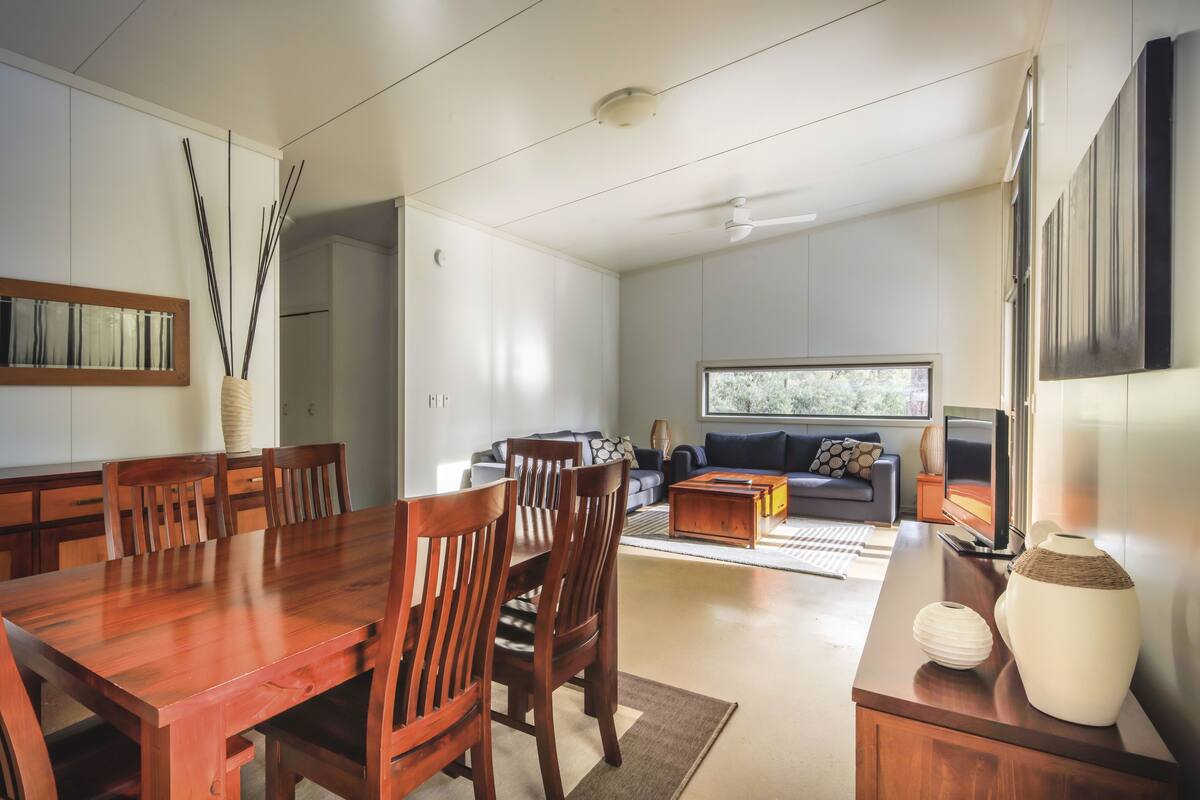 A modern living room with a wooden dining table, chairs, a sofa, and a TV.