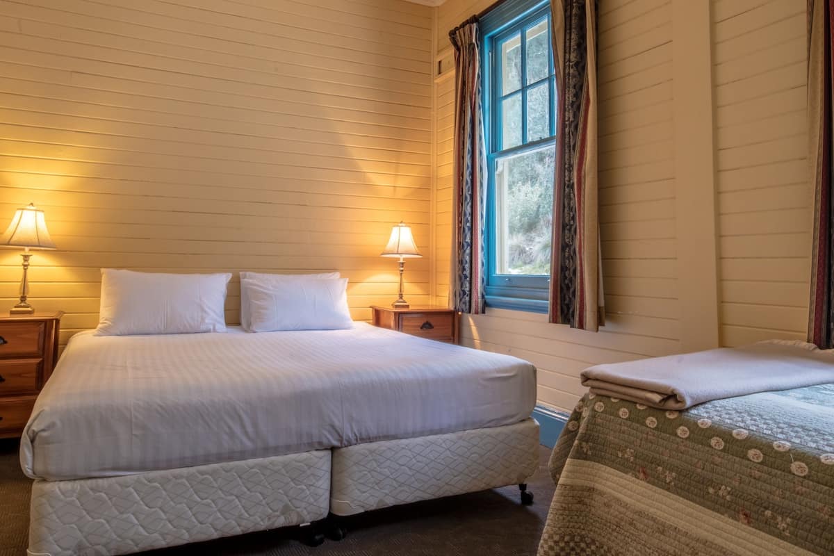 A double bed with white bedding, a bedside table with a lamp, and a window with curtains.