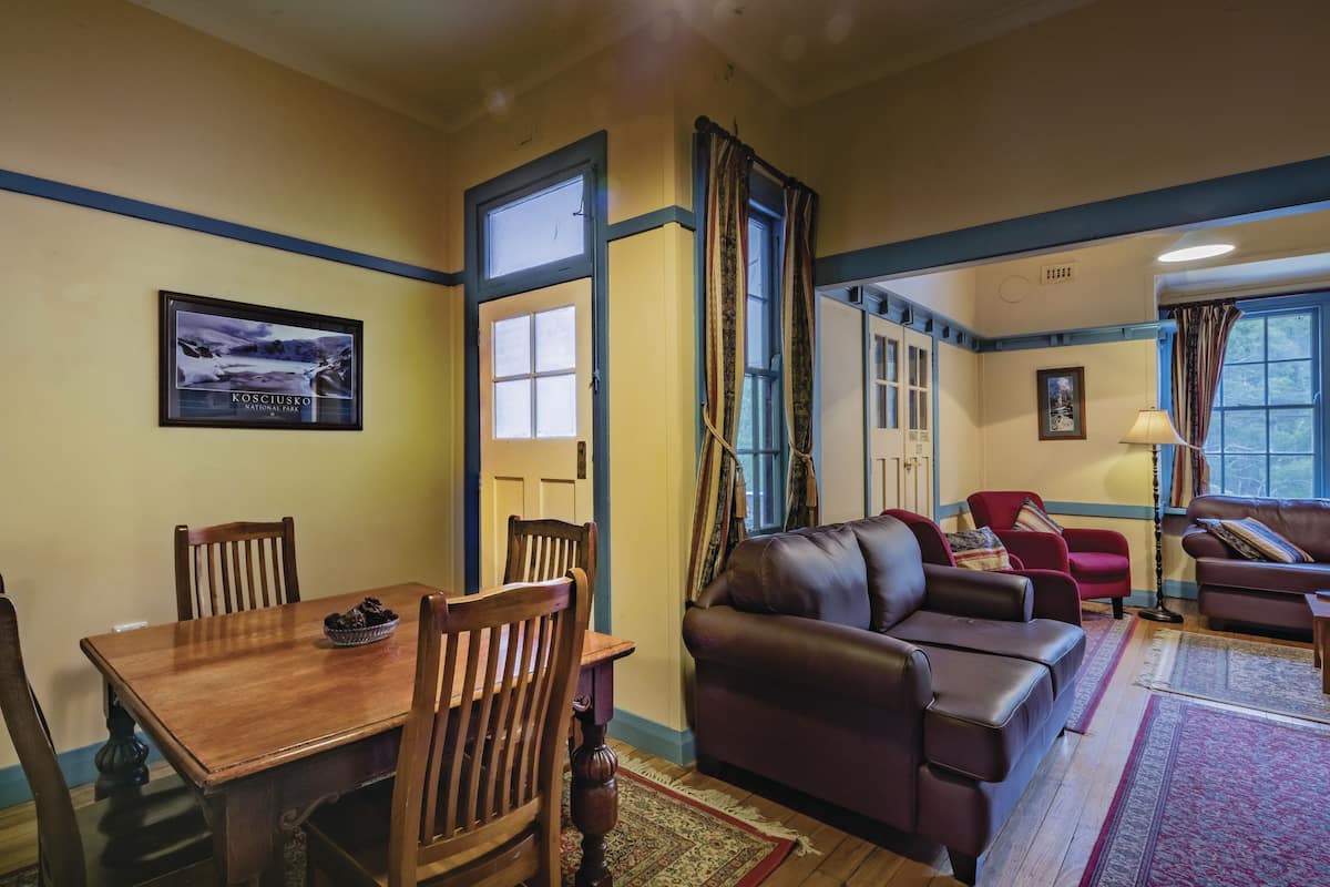 A spacious living room with a wooden dining table, leather sofas, and large windows offering a view of the outdoors.
