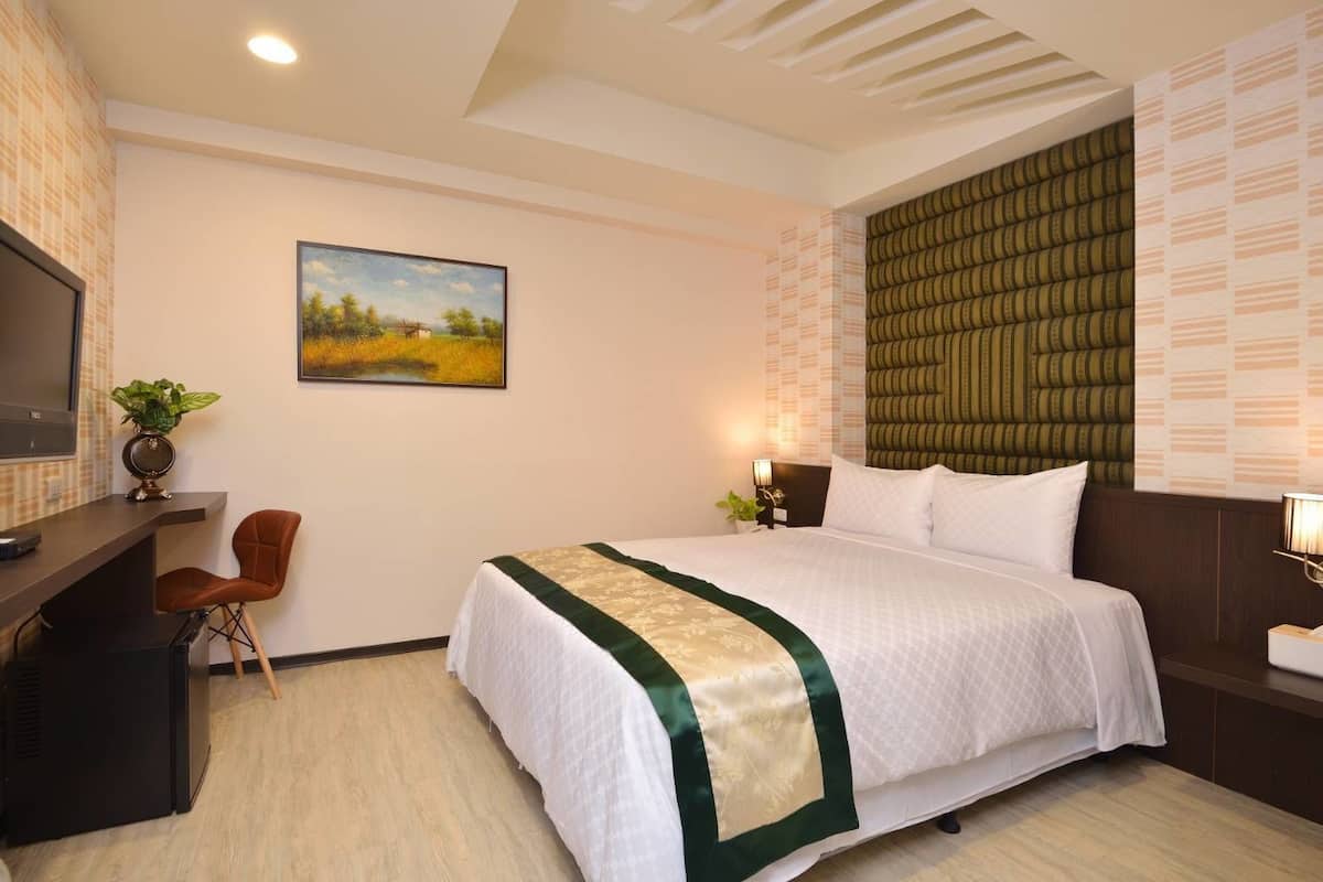 Una habitación de hotel con una cama, un escritorio, una silla, un televisor y un cuadro en la pared.