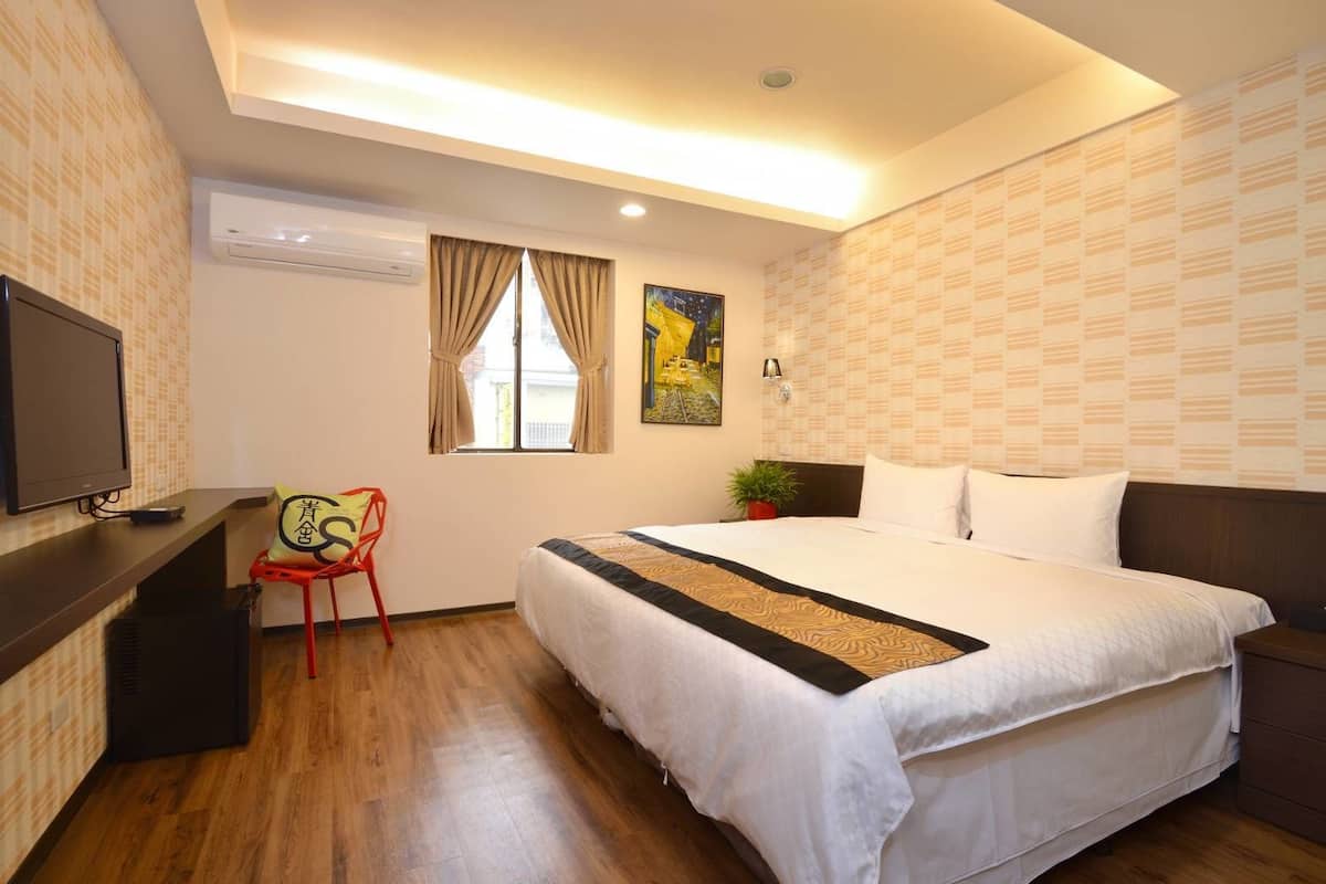 Habitación de hotel con cama, escritorio con televisor, silla y ventana con cortinas.