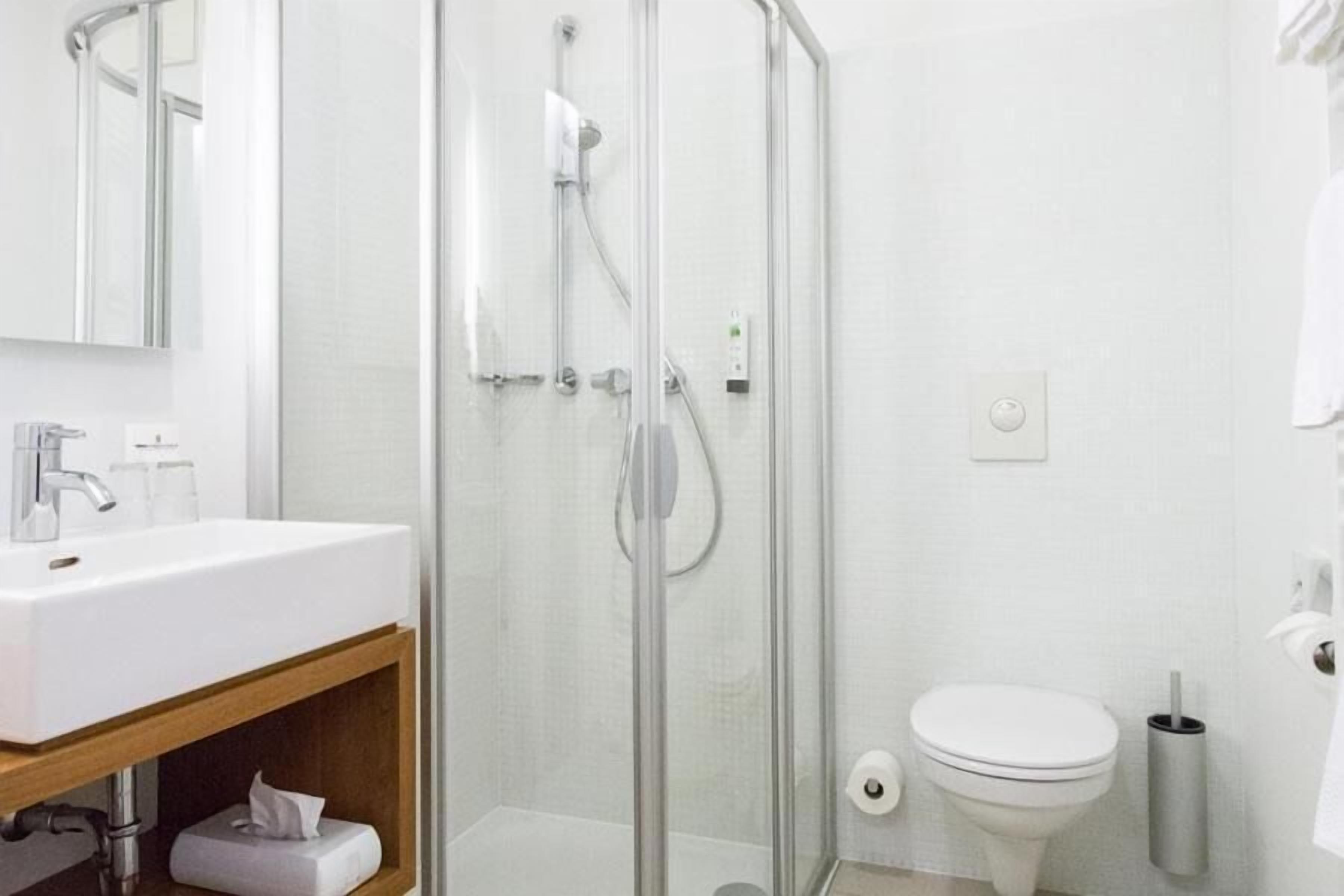Un baño moderno con ducha de vidrio, un lavamanos blanco y un inodoro.