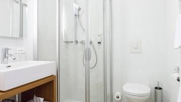 Un baño moderno con ducha de vidrio, un lavamanos blanco y un inodoro.