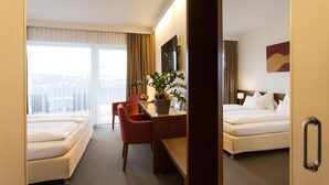 Habitación de hotel con dos camas, un escritorio, una silla, una planta en maceta y vistas a la ciudad.