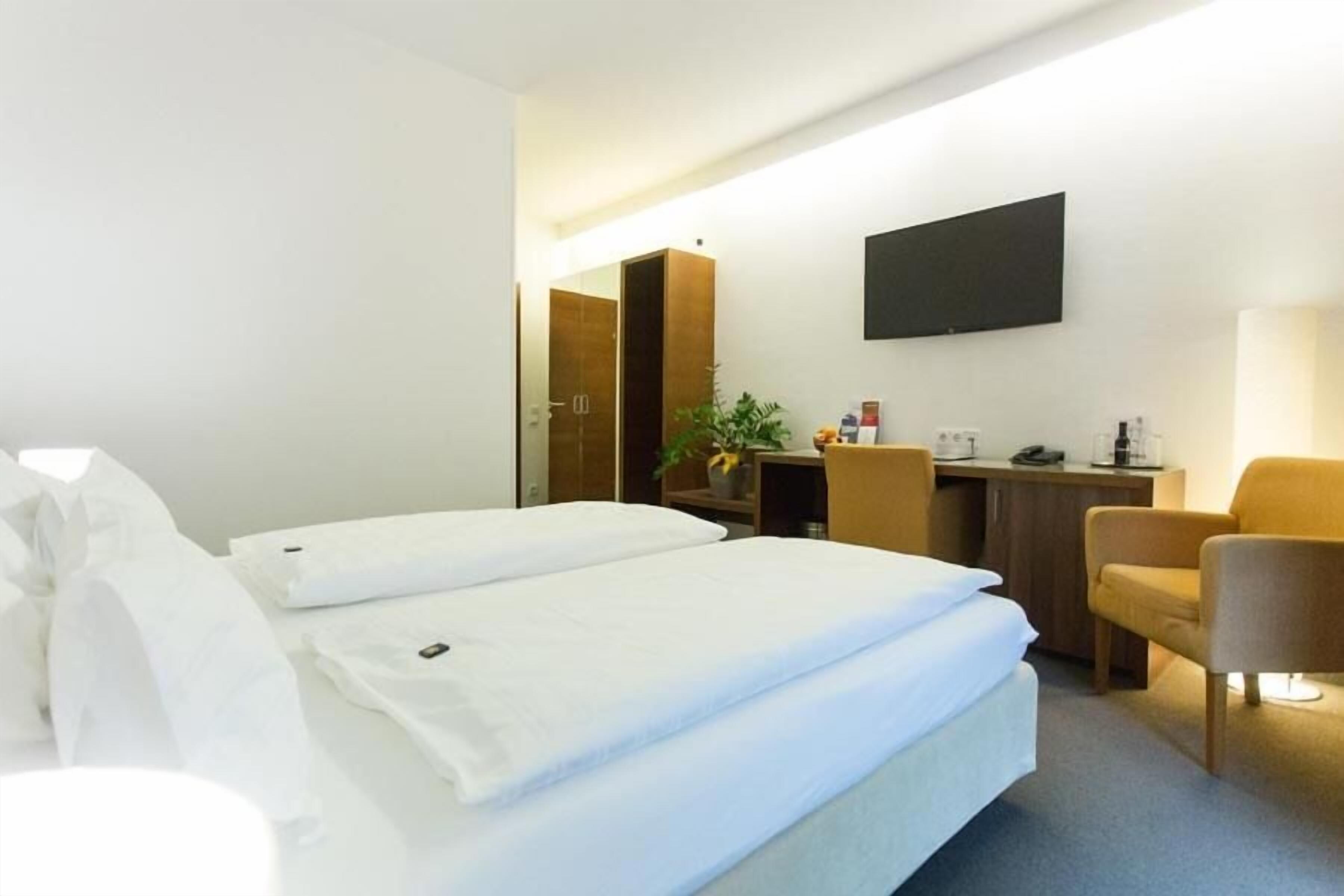 A hotel room with two beds, a desk, a chair, and a TV on the wall.