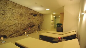 Un área de spa con mesas de masaje, velas y una pared de rocas.