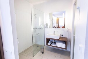 Un baño moderno con cabina de ducha de vidrio, un lavabo blanco con tocador de madera y un espejo sobre el lavabo.