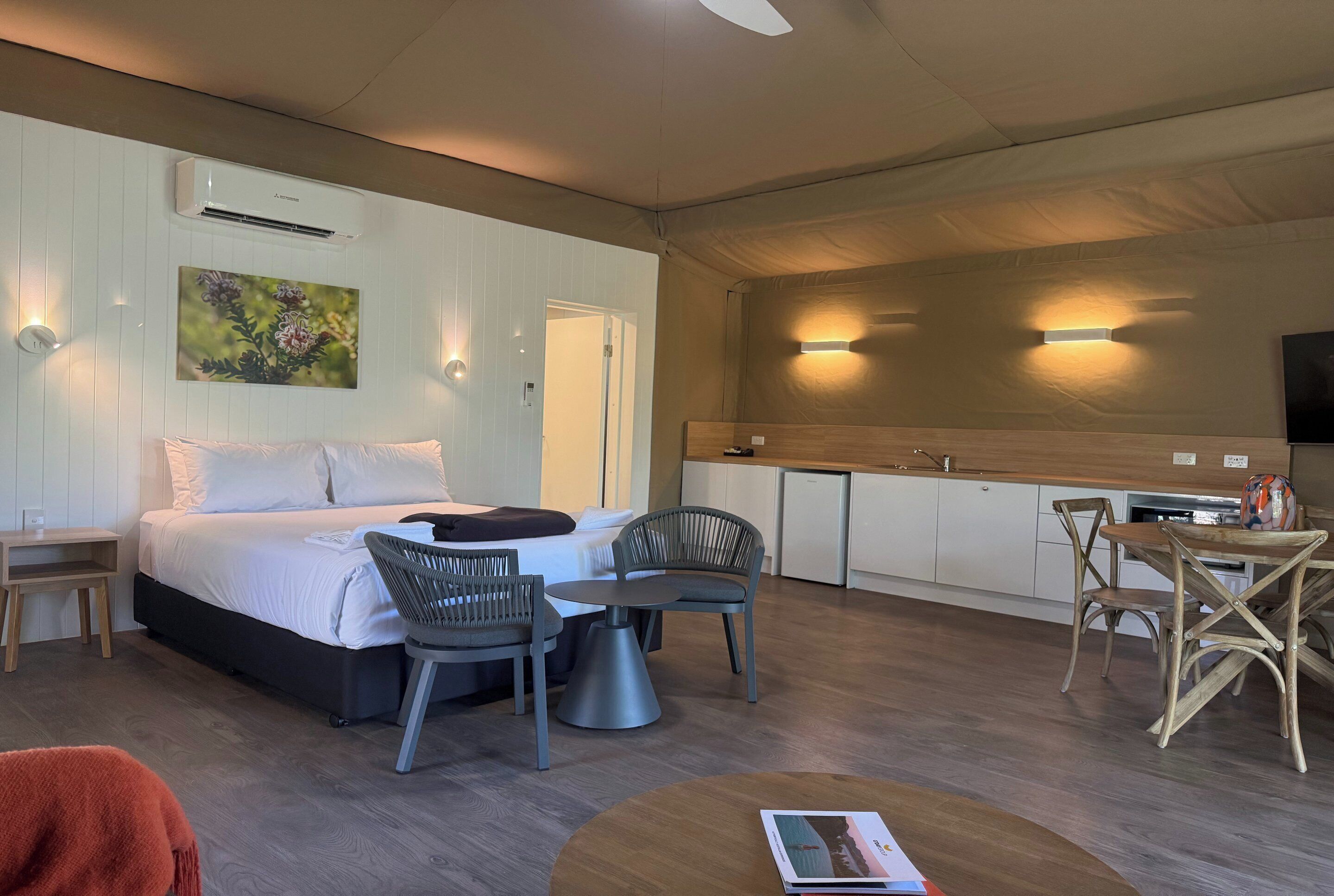 A hotel room with a bed, a desk, a chair, a dining table, and a kitchen area.