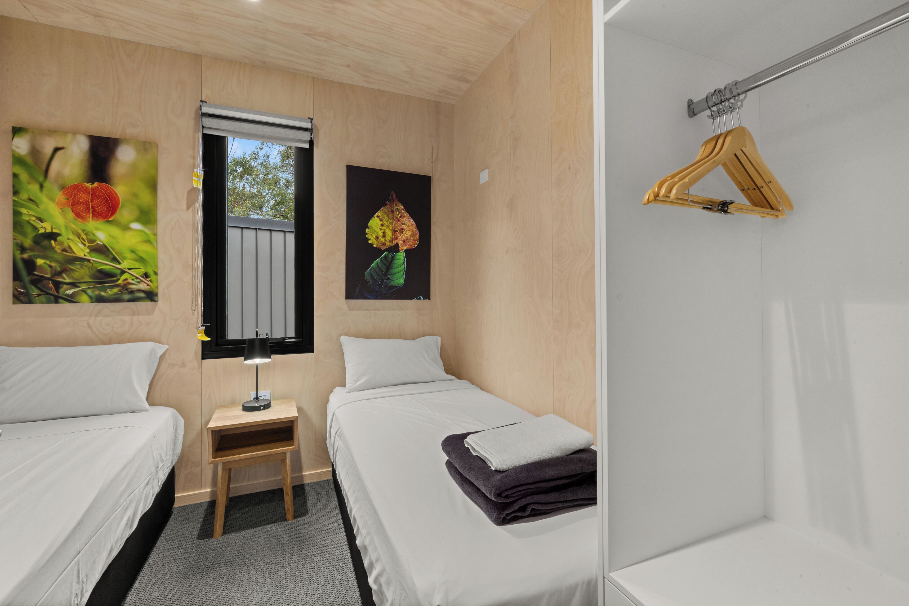 Een hotelkamer met twee bedden, een kleine tafel met een lamp en een houten kapstok aan de muur.