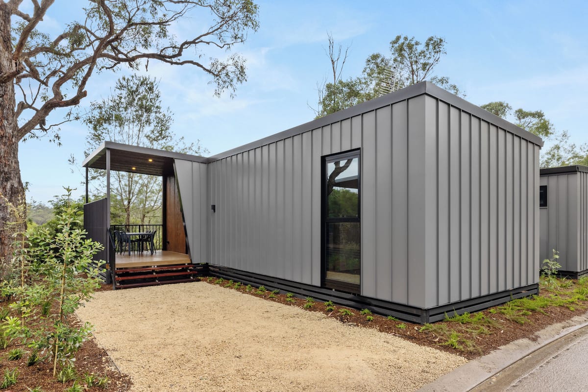 A modern, single-story building with a flat roof, large windows, and a covered outdoor seating area.
