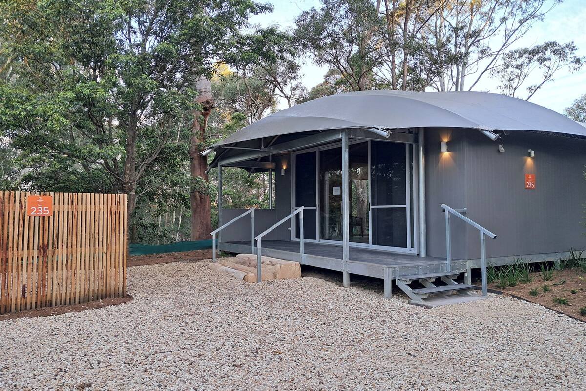 A modern building with a covered outdoor area, a wooden fence, and a gravel ground.