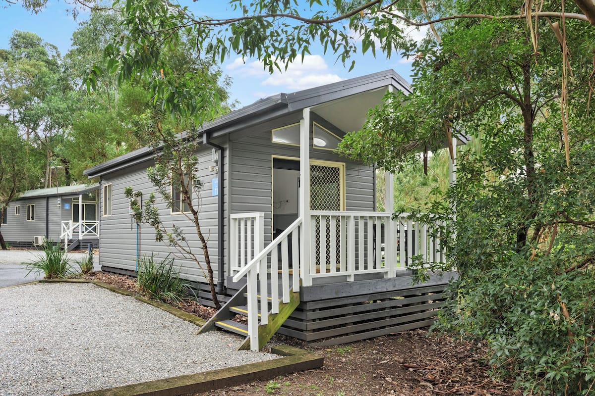 A small, single-story cabin with a front porch and a staircase leading to the entrance.