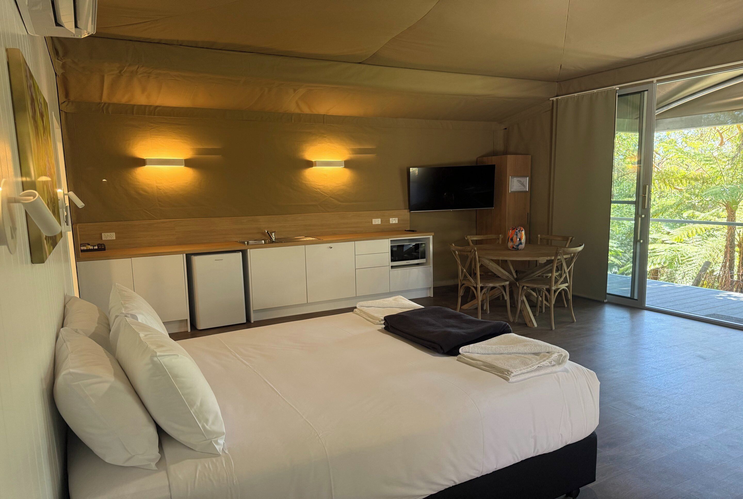 Une chambre d’hôtel moderne dotée d’un grand lit, d’une table à manger, d’un téléviseur à écran plat et d’une porte-fenêtre coulissante donnant sur l’extérieur.