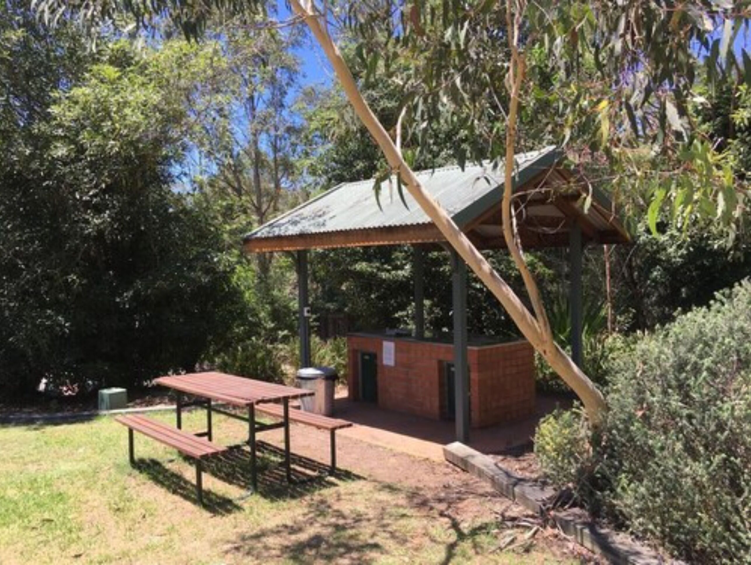 Ein Picknickplatz mit Metallunterstand, einem Picknicktisch und einem Mülleimer.