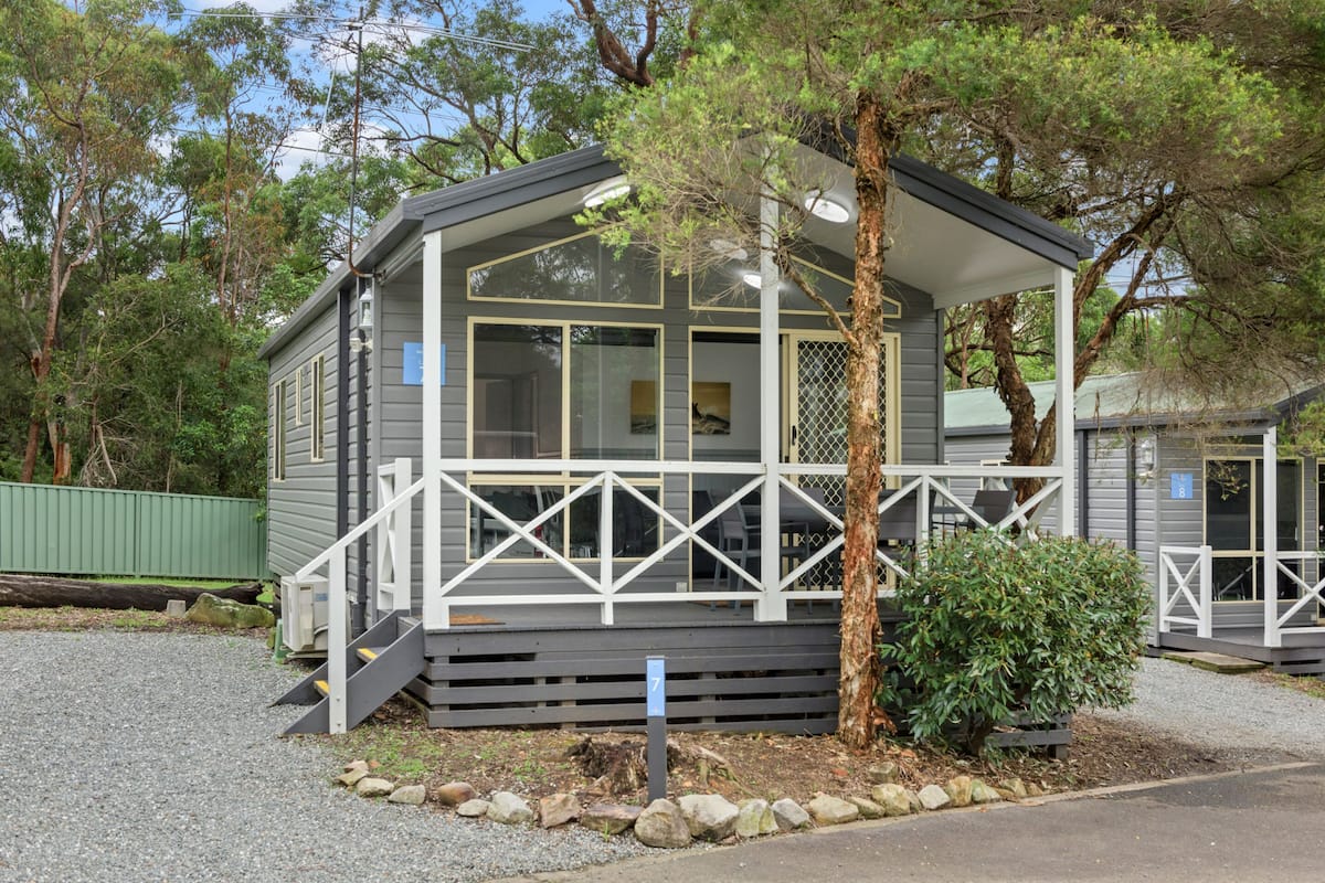 A small, single-story cabin with a porch and a covered outdoor seating area.