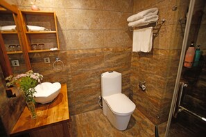 Une salle de bain avec un mur en marbre, un meuble-lavabo en bois, un lavabo blanc, des toilettes et une cabine de douche en verre.