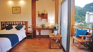 Ein Hotelzimmer mit einem Bett, einem kleinen Tisch mit Lampe und Blick auf eine Berglandschaft.