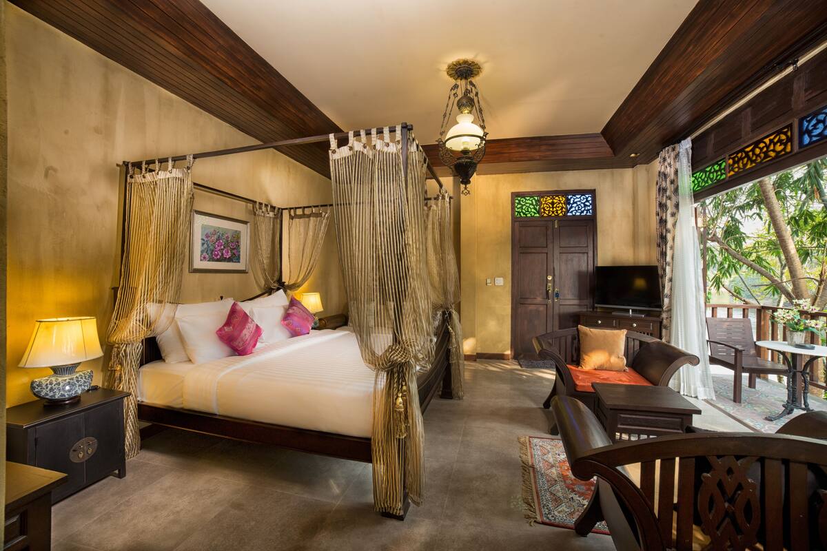 A bedroom with a four-poster bed, a television, and a seating area with a table and chairs.