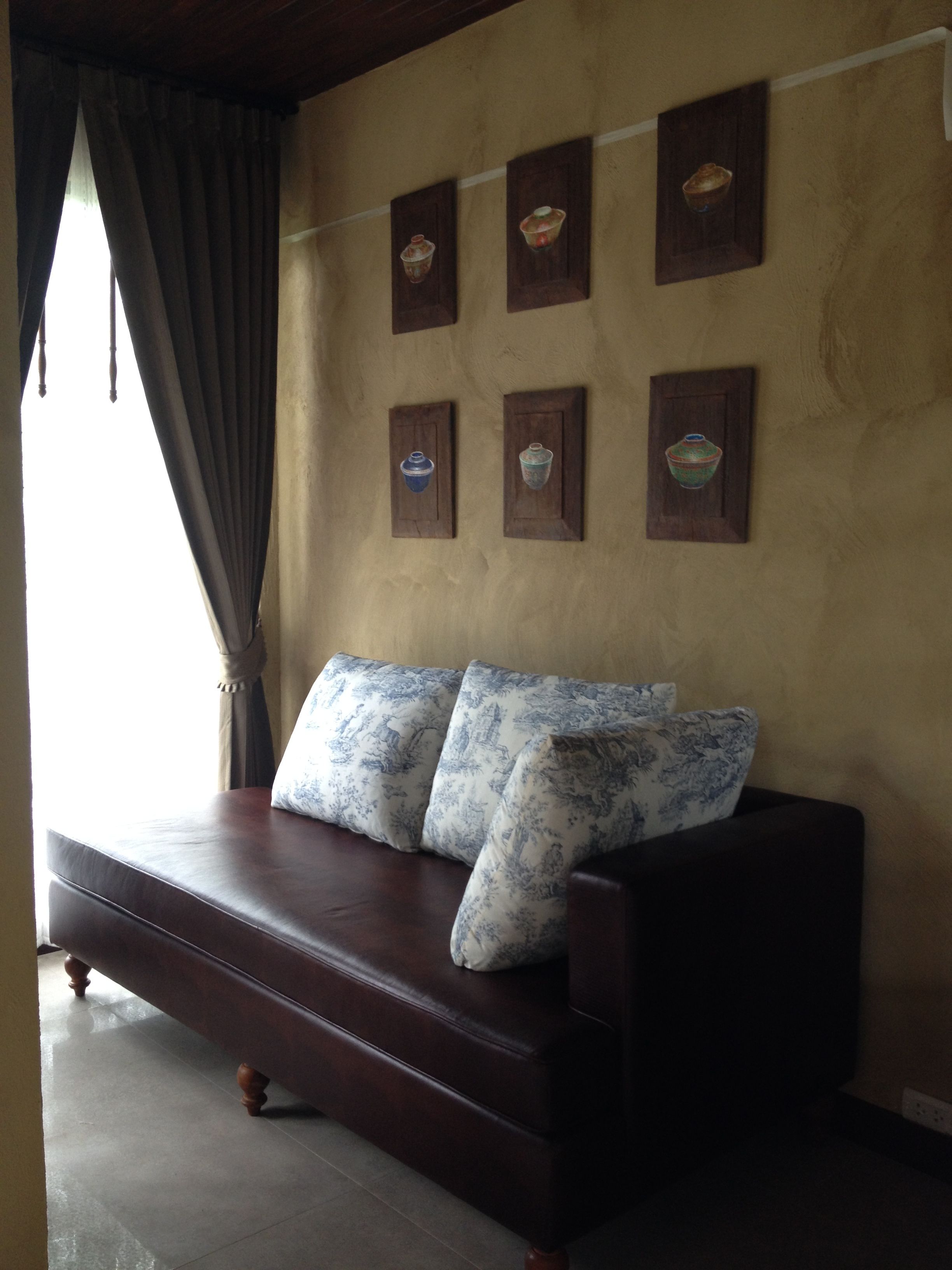A room with a brown leather sofa, two patterned cushions, and six framed ceramic vases on the wall.