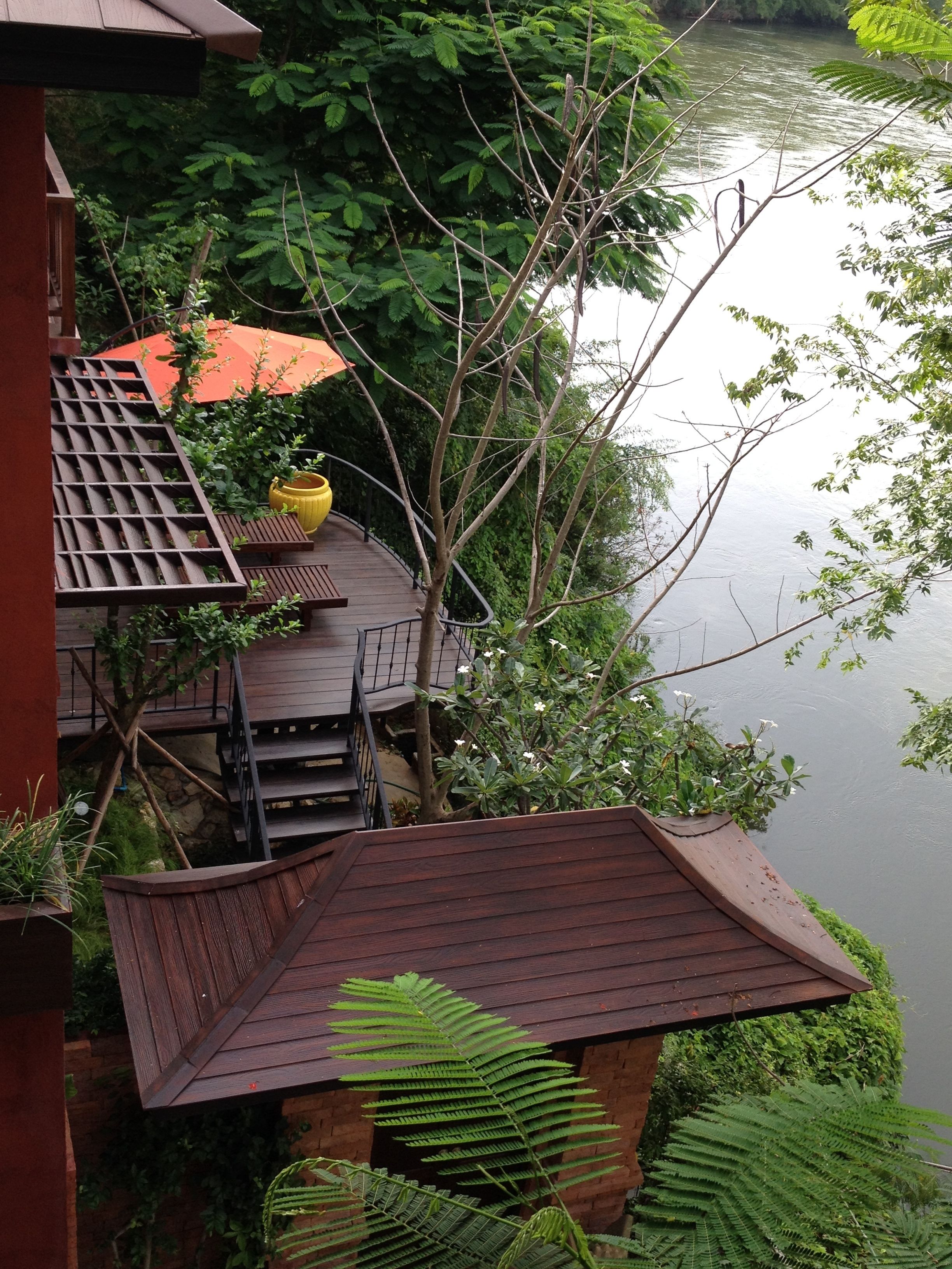 A wooden deck with a railing overlooking a body of water, surrounded by lush greenery.