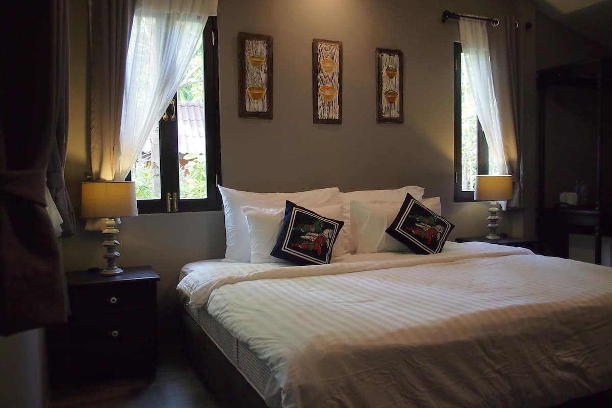 A neatly made bed with white linens and two decorative pillows, a bedside table with a lamp, and three wall-mounted artwork pieces.
