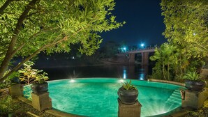 Een zwembad bij nacht, omringd door bomen, met een brug op de achtergrond.