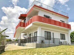 A two-story building with a red and white facade, balconies, and a concrete pathway leading to the entrance. - Okinawa Pension Minami (Nanjo)