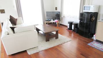 Uma sala de estar com sofá, mesa de centro, televisão e geladeira.