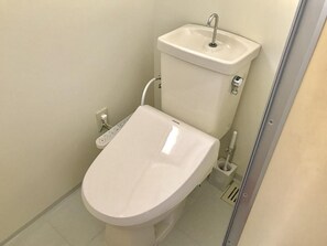 A modern bathroom with a white toilet, a wall-mounted sink, and a handheld bidet. - Okinawa Pension Minami (Nanjo)