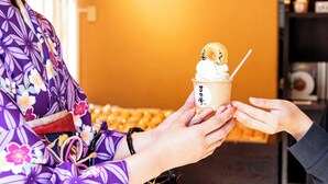 A person holding a cup of ice cream with a spoon, in front of a sign with Japanese characters.