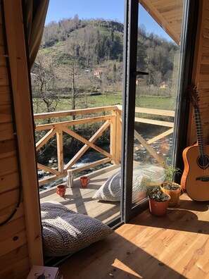 A wooden cabin with a glass door leading to a balcony overlooking a river and a hilly landscape. - Sana Yasam Koyu (Findikli)