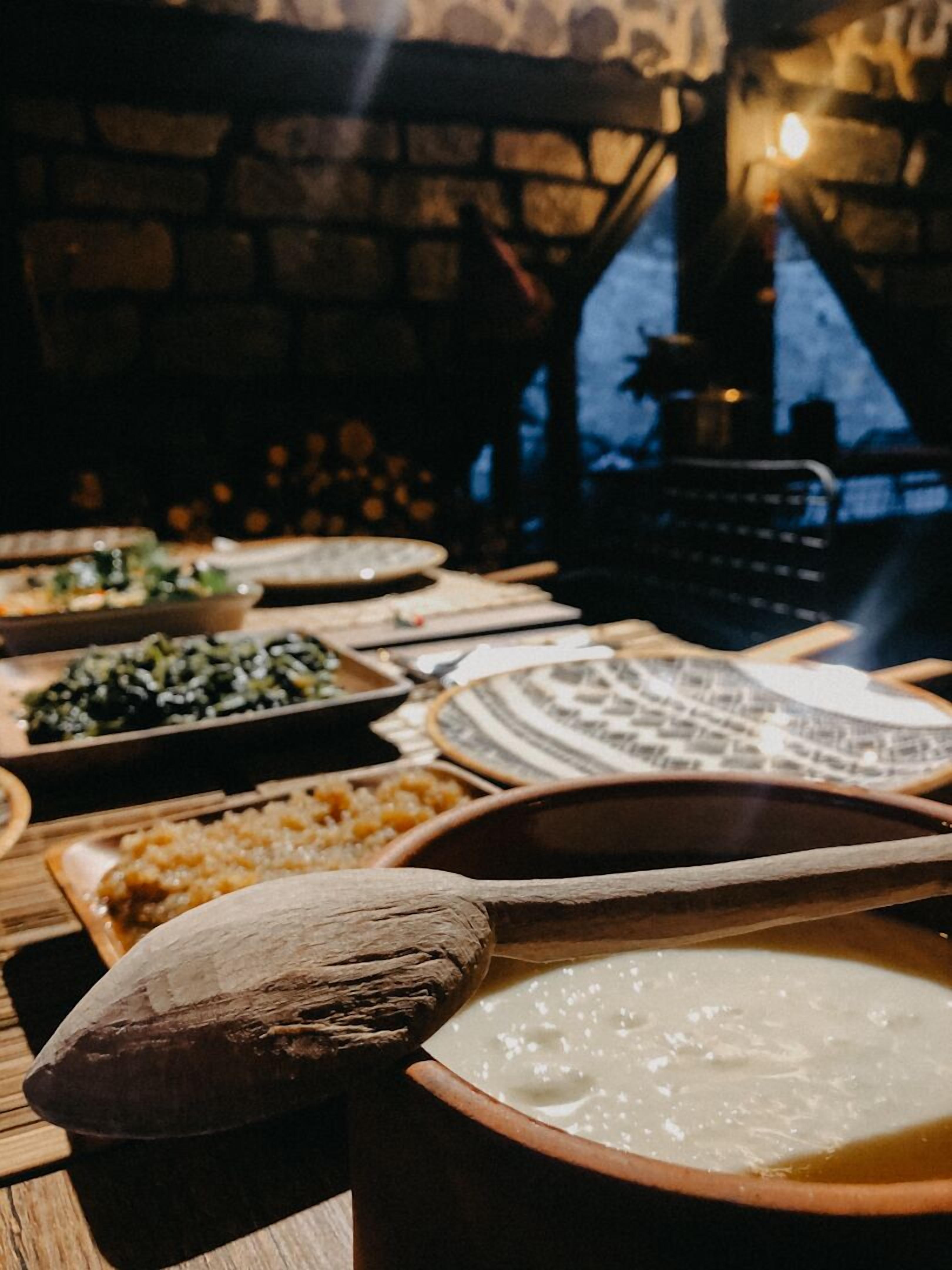 Una mesa con varios platos, incluyendo un tazón de sopa y diferentes acompañamientos, en una habitación poco iluminada con paredes de ladrillo.