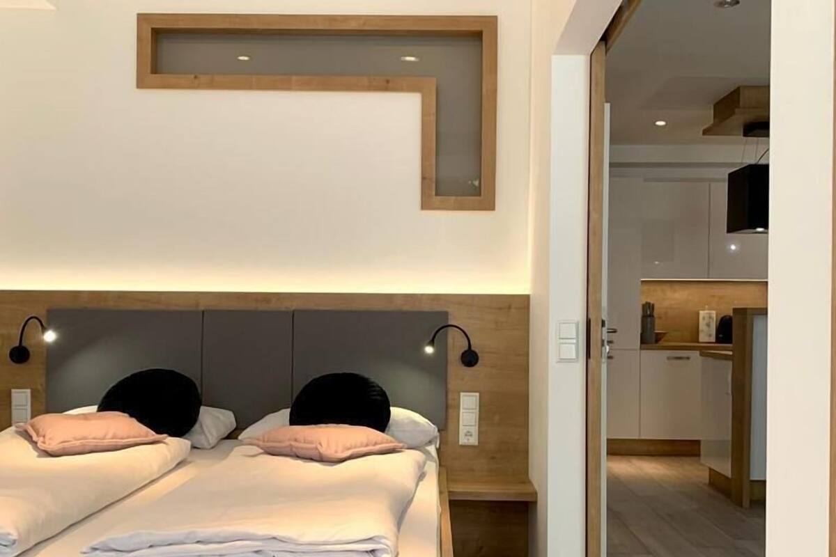 A modern bedroom with a wooden bed frame, two bedside tables, and a built-in headboard.