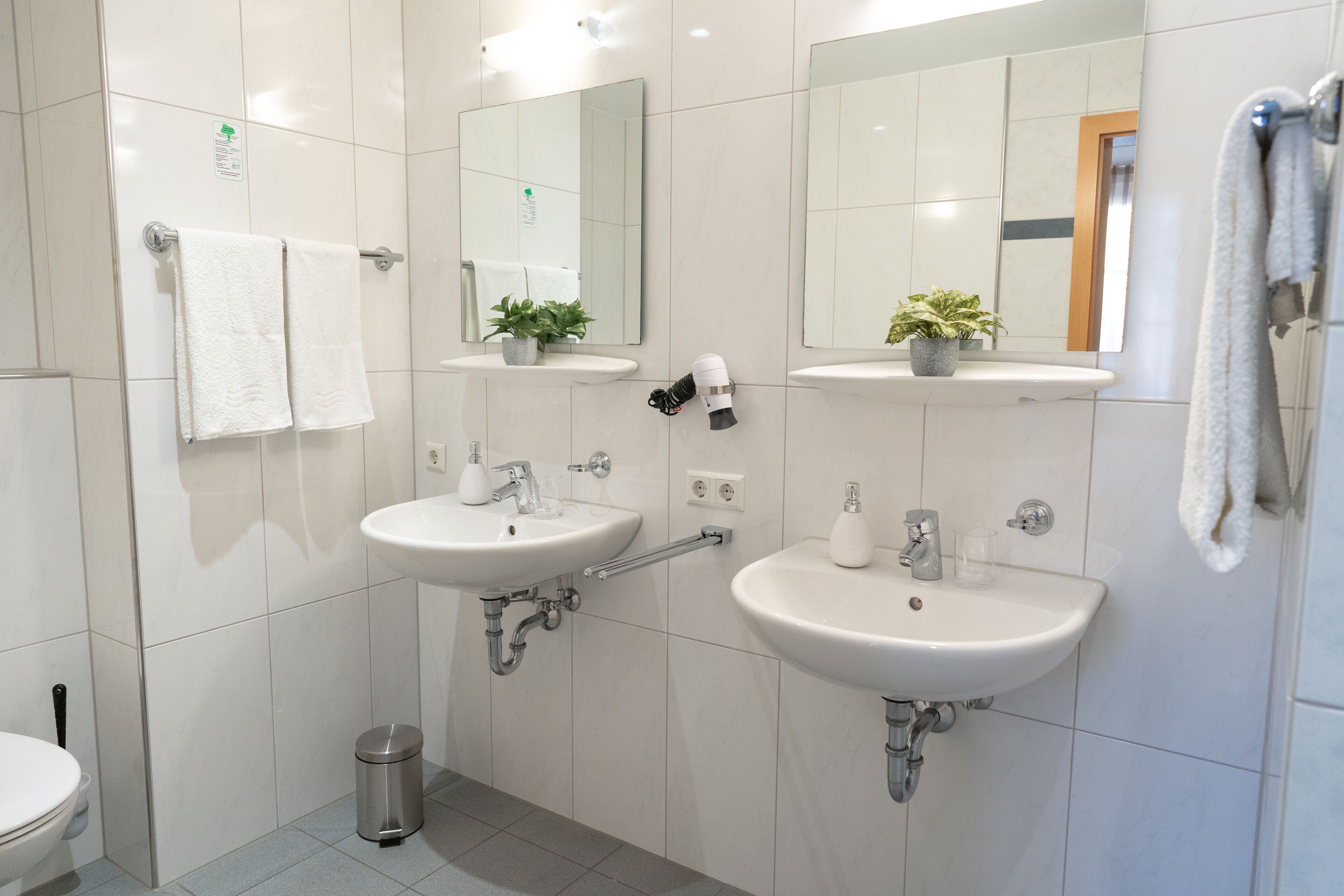 A modern bathroom with two sinks, a mirror, and a small trash can.