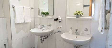 A modern bathroom with two sinks, a mirror, and a small trash can.