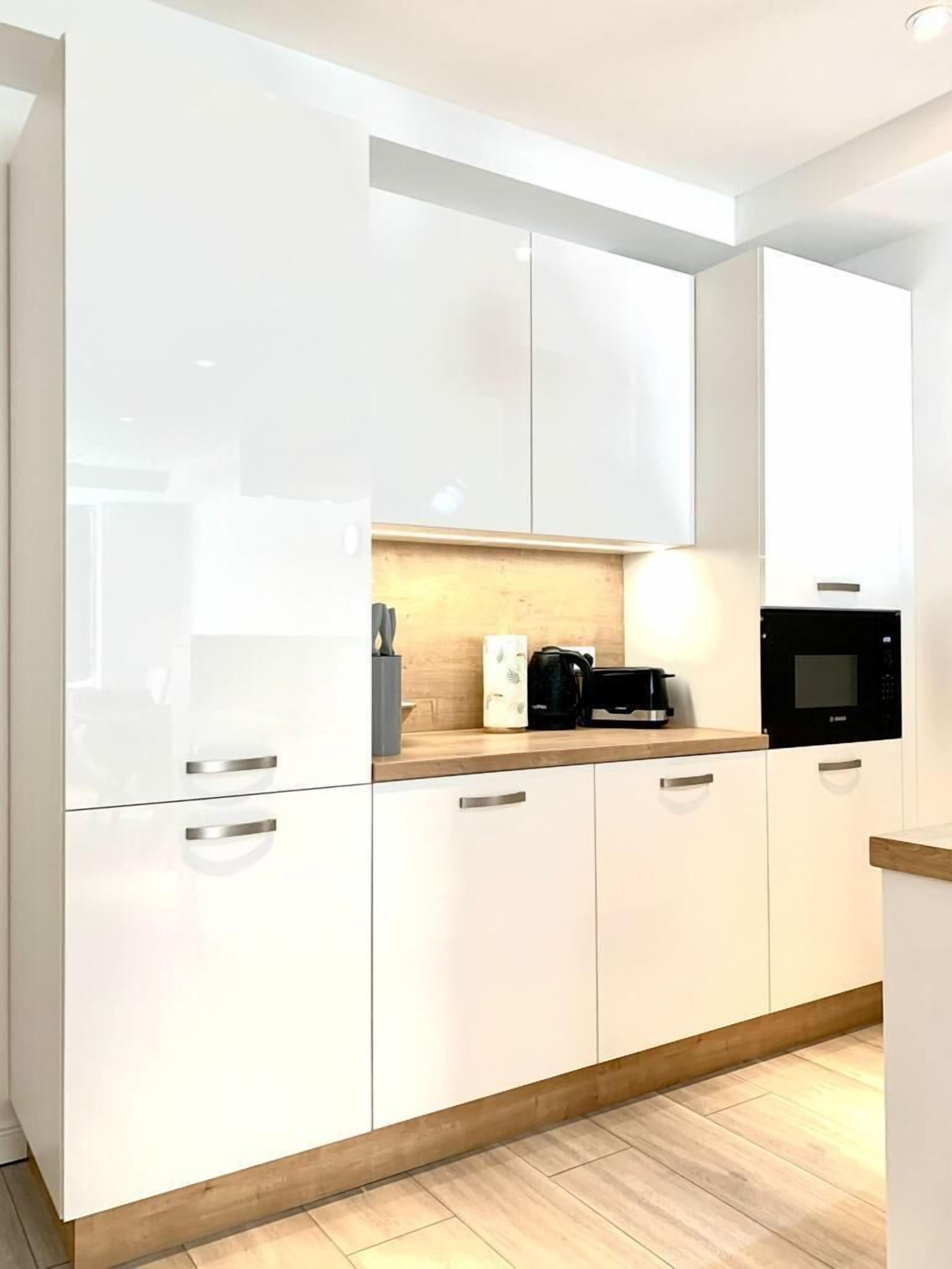 Une cuisine moderne avec des armoires blanches, un plan de travail en bois et un micro-ondes noir.