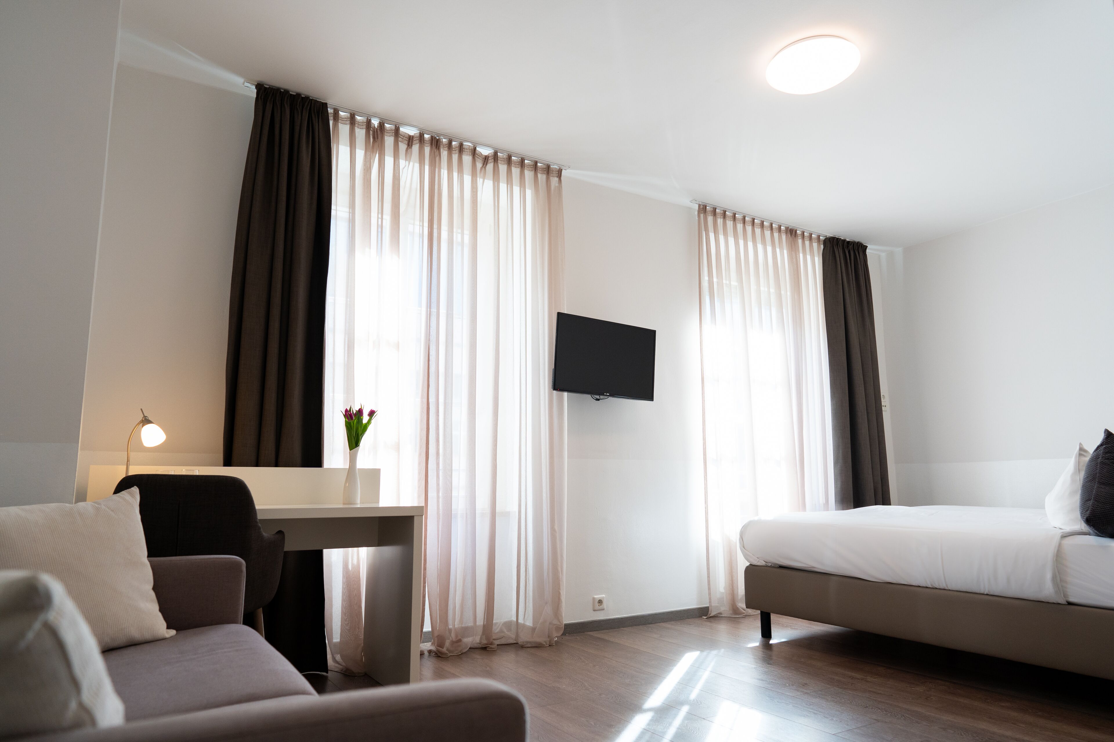 Een hotelkamer met een bed, een bureau, een stoel, een televisie en gordijnen.