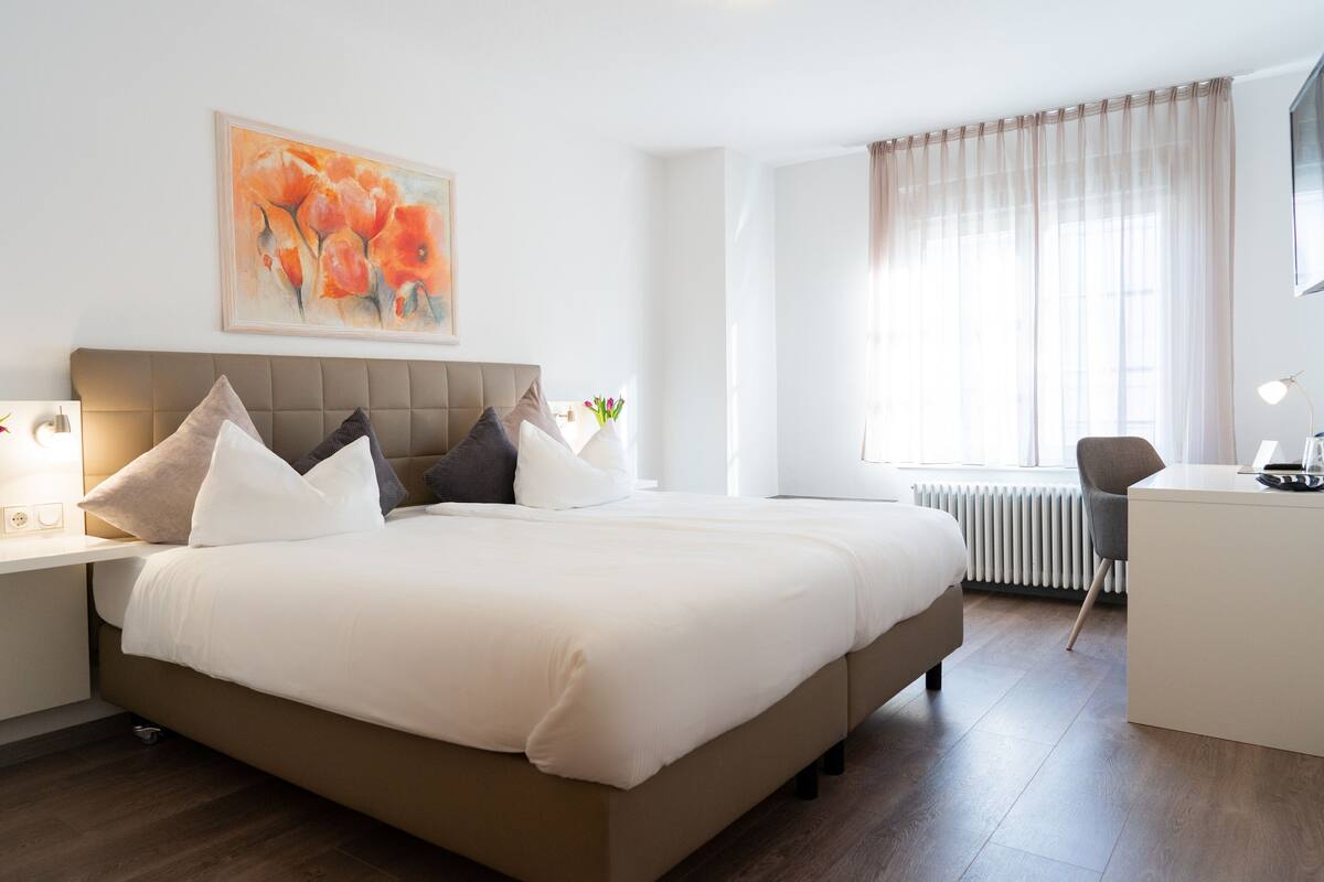 A hotel room with a large bed, bedside tables, a desk, a chair, and a window with curtains.