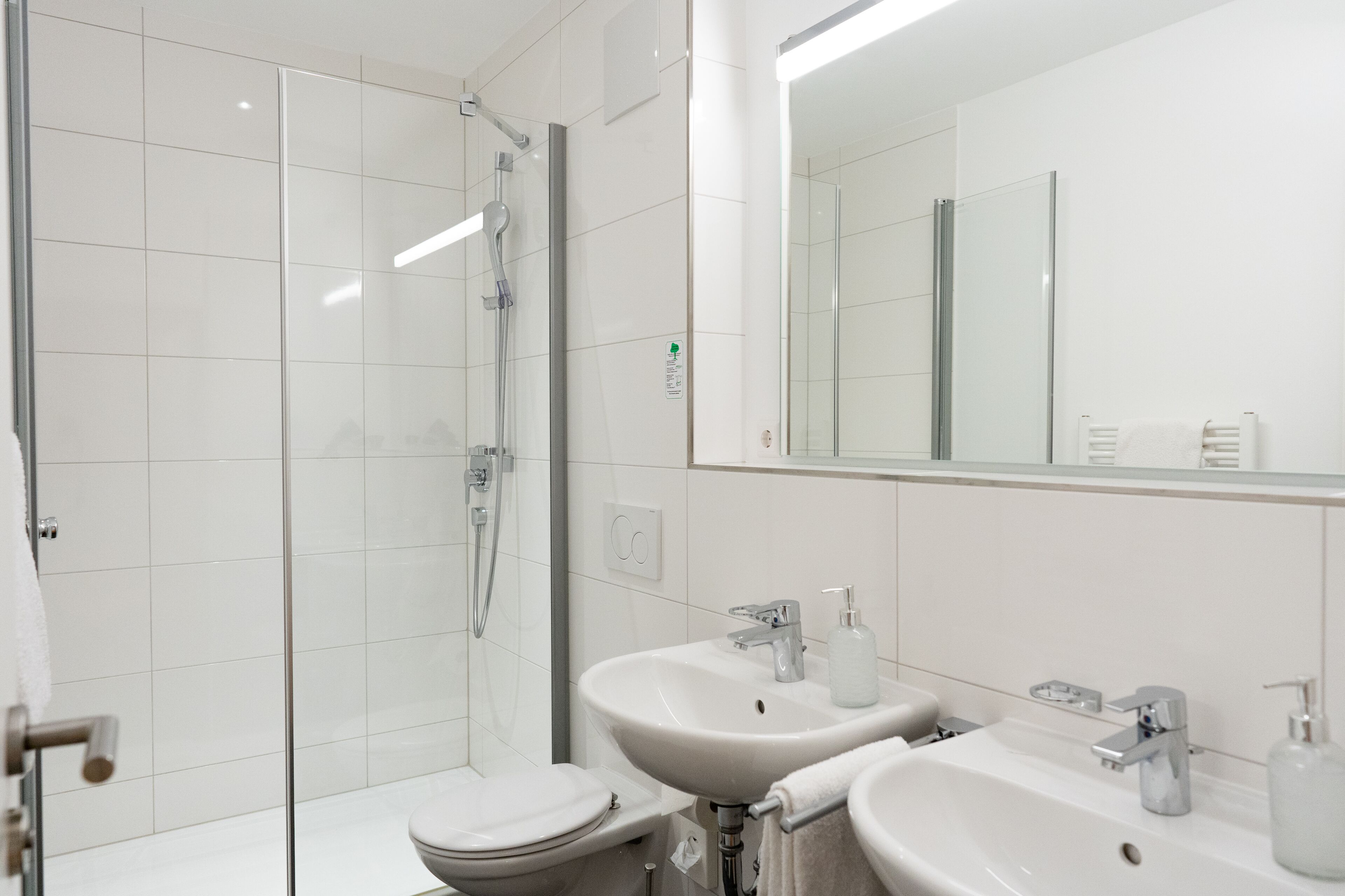 A modern bathroom with a glass shower enclosure, a toilet, and two sinks with mirrors.