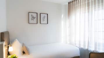 A hotel room with a bed, a bedside lamp, a potted plant, and two framed pictures on the wall.