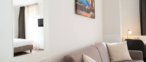 Una habitación de hotel moderna con una cama grande, un sofá, un cuadro en la pared y una mesita de noche con una lámpara.