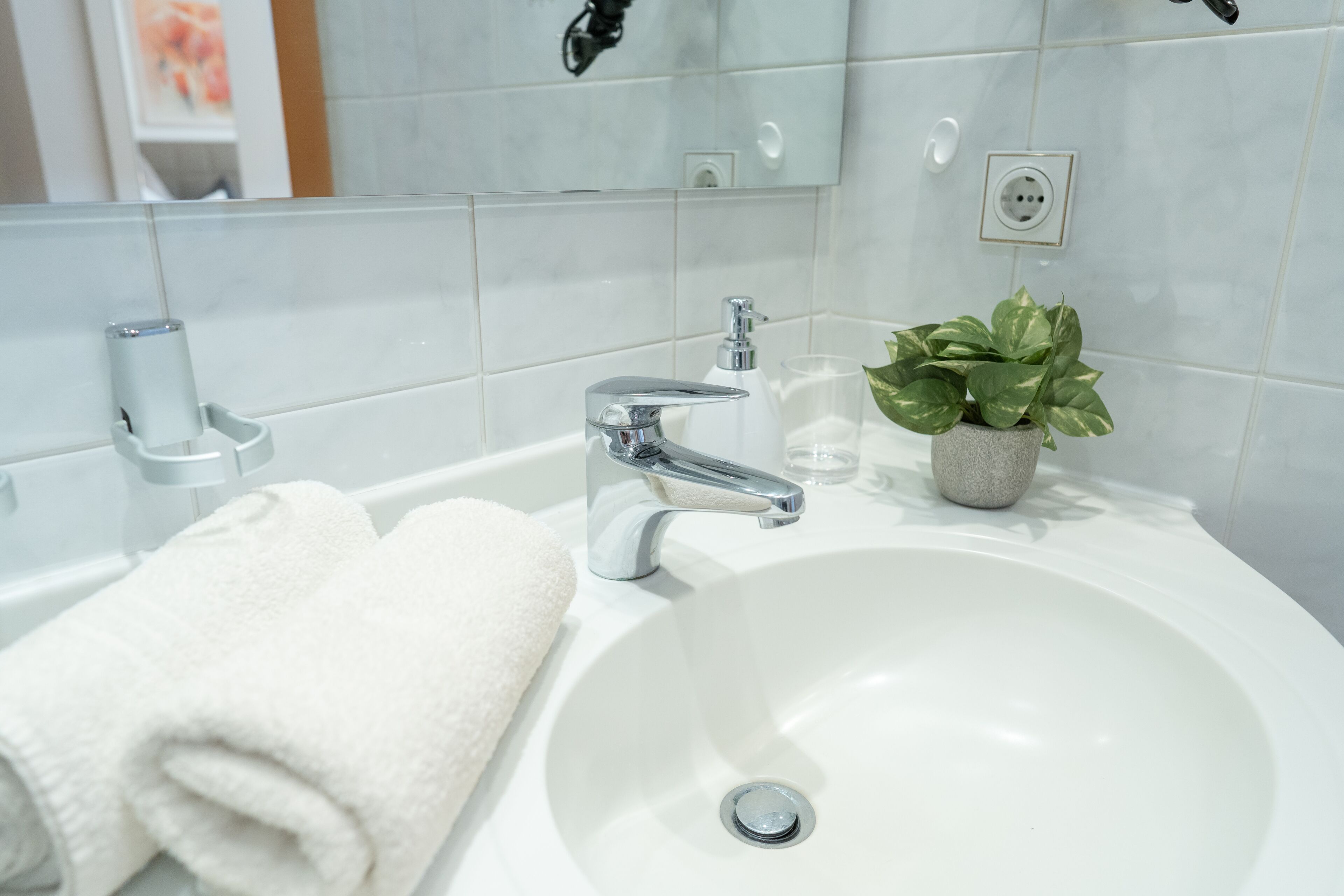 A white bathroom sink with a chrome faucet, a white towel, and a potted plant.
