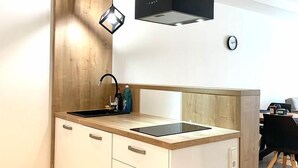 A modern kitchen with a wooden accent wall, a black pendant light, and a built-in stove. - Hotel La Fleur (Ueberlingen)